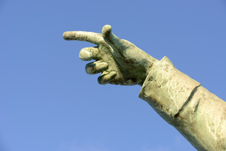 a stone statue hand with finger pointing on a blue sky backgroundの写真素材