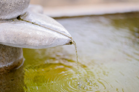 Close-up of Water Droplet Falling from Stone Fountain Sculpture with Ripplesの写真素材