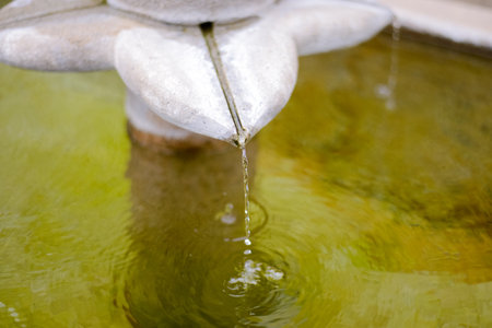 Close-up of Water Droplet Falling from Stone Fountain Sculpture with Ripplesの写真素材