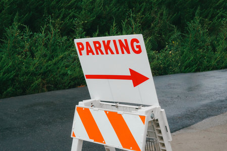 Parking Guide Sign with Red 'PARKING' Text and Arrow Set Against a Background of Dark Green Bushesの写真素材