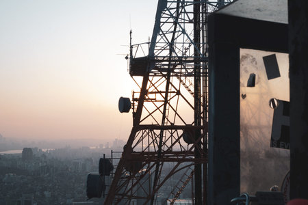 Communication Tower Structure Silhouette Against a City Sunsetの写真素材