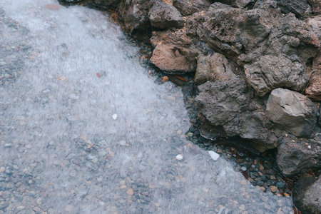 Transparent Ice Surface of a Frozen Lake or Puddle Bordering Rough Basalt Rocksの写真素材