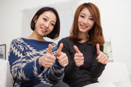 Two young Asian woman show thumb in home background の写真素材