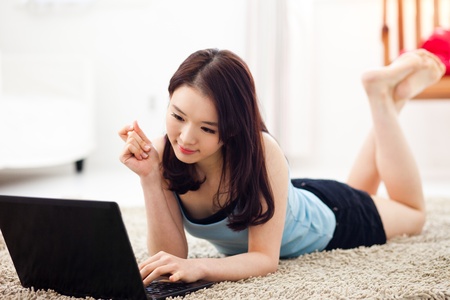 Young Asian woman using laptop lying down.の写真素材