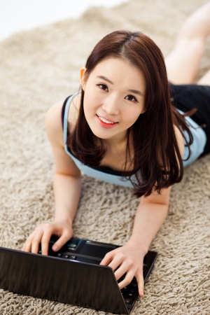 Young Asian woman using laptop lying down.の写真素材