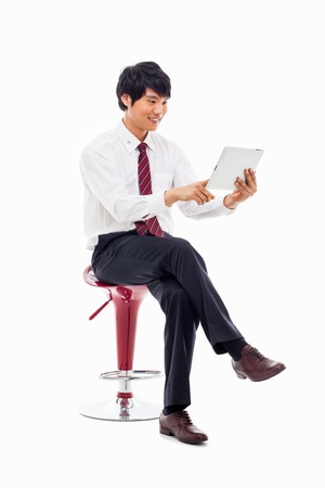 Young Asian business man using a pad PC sitting on the chair isolated on white background. の写真素材