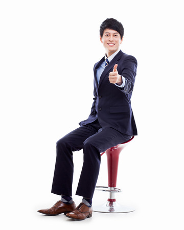 Young Asian business man sitting on the chair and showing thumbの写真素材