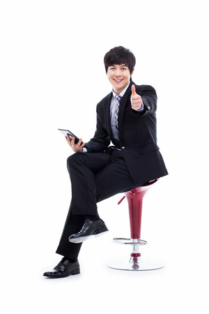 Young Asian business man sitting on the chair and showing thumb isolated on white background. の写真素材