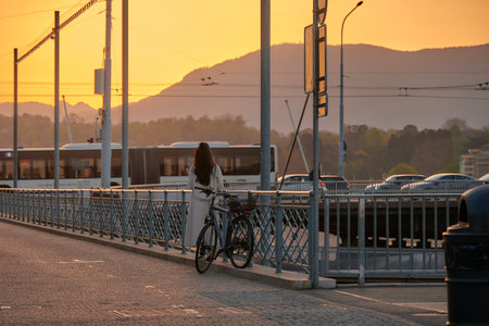 GENEVA, SWITZERLAND - 14 APRIL,2022: A women park her bike and look at the sunrise in Geneva with busy traffic.の写真素材