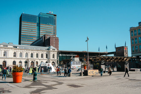 Oslo, Norway - Apr 13, 2024: An urban square in Oslo, Norway, featuring modern and historical buildings. People are walking around, enjoying the sunny day.の写真素材
