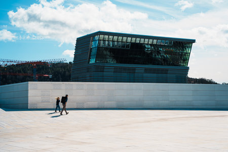 Oslo, Norway - Apr 13, 2024: People walking and relaxing at Oslo Opera House, A modern architectural building with sloped roof by the waterfront.の写真素材