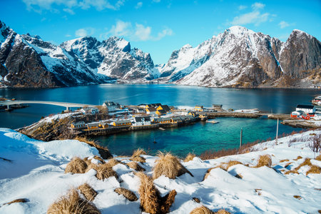 A picturesque Sarkisoy village nestled by the fjord, surrounded by snow-capped mountains under a clear blue sky.の写真素材