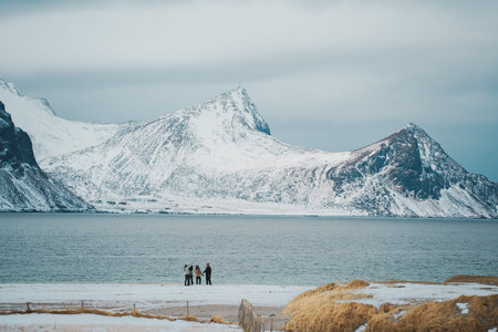 Scenic winter landscape at Haukland beach in Lofoten, Norway, featuring snow-covered peaks, calm...