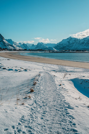 Winter landscape of Ramberg Beach on Lofoten Island, Norway, with snow-covered shoreline, Arctic waters, and dramatic mountain peaks.の写真素材