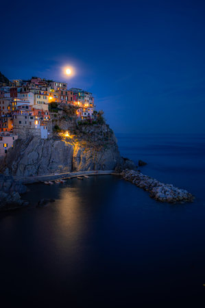 Magical view of Manarola on a moonlit night, with glowing village lights reflecting over calm Ligurian waters in Cinque Terre.の写真素材