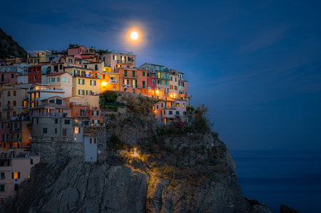 Magical view of Manarola on a moonlit night, with glowing village lights reflecting over calm Ligurian waters in Cinque Terre.の写真素材