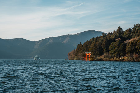 Scenic view of a traditional red torii gate standing in Lake Ashi with forested hills in the background.の写真素材