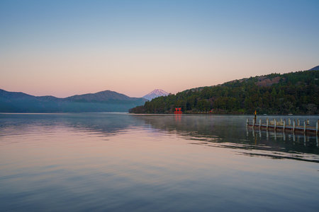 Scenic view of Mount Fuji behind lush forest and iconic red torii gate at Lake Ashi in Hakone, Japan...