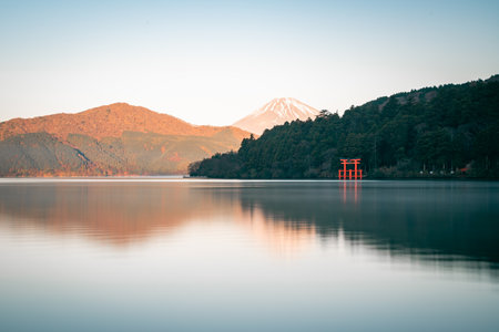 Scenic view of Mount Fuji behind lush forest and iconic red torii gate at Lake Ashi in Hakone, Japan during sunrise.の写真素材