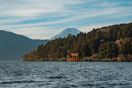 Scenic view of a traditional red torii gate standing in a lake with forested hills in the background.の写真素材