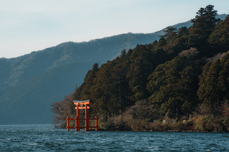 Scenic view of a traditional red torii gate standing in a lake with forested hills in the background.の写真素材