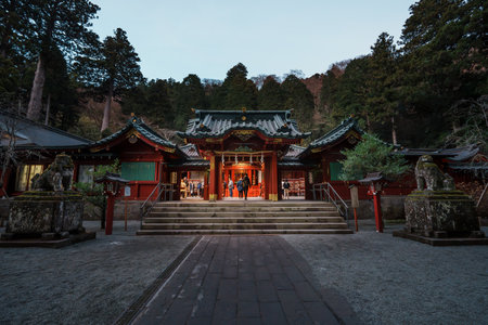 Hakone, Japan - Dec 9, 2023: Twilight view of Hakone Shrine with traditional red architecture, visitors exploring sacred grounds surrounded by tall cedar trees.の写真素材