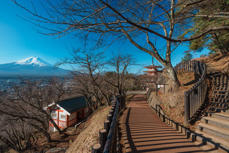 A winding path leads past a shrine building towards the iconic Chureito Pagoda with Mount Fuji in...