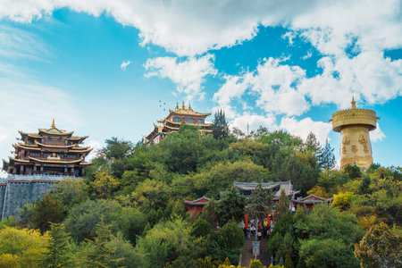 Traditional temples and the enormous golden prayer wheel crown a lush hillside in Guishan Park,...