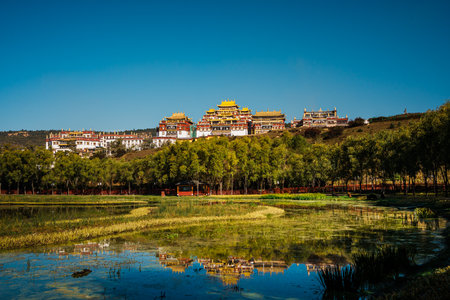 The stunning Ganden Sumtseling Monastery sits on a hill reflected in a calm lake, showcasing a classic view of Shangri la.の写真素材