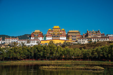 The stunning Ganden Sumtseling Monastery sits on a hill reflected in a calm lake, showcasing a classic view of Shangri la.の写真素材