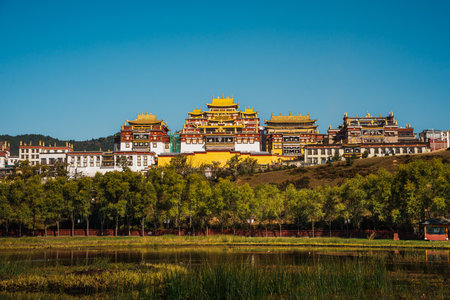The stunning Ganden Sumtseling Monastery sits on a hill reflected in a calm lake, showcasing a classic view of Shangri la.の写真素材