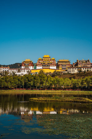 The stunning Ganden Sumtseling Monastery sits on a hill reflected in a calm lake, showcasing a classic view of Shangri la.の写真素材