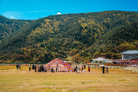 A wide, panoramic landscape showing the immense scale of the Yila Grassland and Napahai Lake, with people scattered across the plain.の写真素材