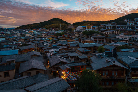 Dramatic pink and blue sunset clouds over the historic rooftops and mountains of Dukezong Ancient Town in Yunnan, China.の写真素材