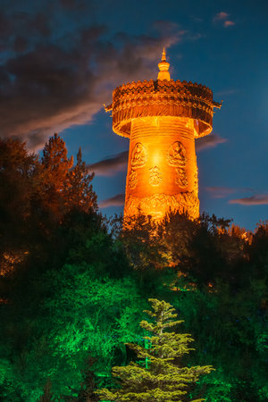 Golden light bathes the giant prayer wheel of Dafo Temple on Guishan Hill against a deep blue twilight sky in Yunnan, China.の写真素材