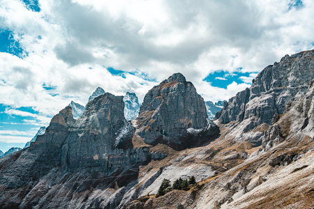 Jagged and dramatic mountain range with sparse snow under a cloudy blue sky.の写真素材