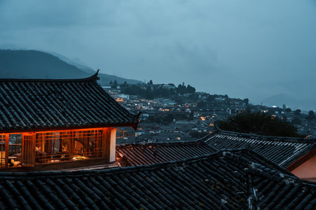 Evening scene over Lijiang Old Town rooftops with glowing warm lights and misty mountains in the background.の写真素材
