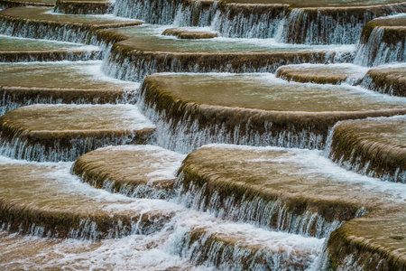 Scenic terraced waterfalls flowing into turquoise pools at Blue Moon Valley, surrounded by lush green hills and misty skies.の写真素材