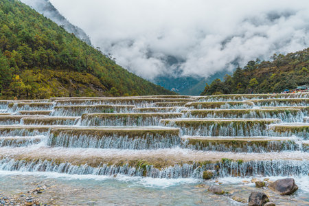 Scenic terraced waterfalls flowing into turquoise pools at Blue Moon Valley, surrounded by lush green hills and misty skies.の写真素材