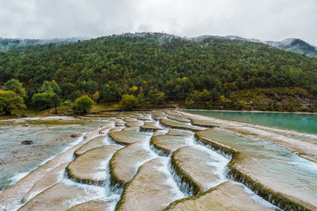 Scenic terraced waterfalls flowing into turquoise pools at Blue Moon Valley, surrounded by lush green hills and misty skies.の写真素材