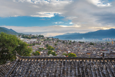 Scenic view of traditional tiled rooftops with distant mountains and a cloudy sky from Lijiang Old Town, Yunnan.の写真素材