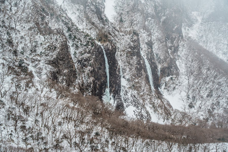 Dramatic snow-covered cliffs and frozen waterfalls shrouded in mist on Yeongsil Trail, Hallasan, Jeju Island, South Korea.の写真素材