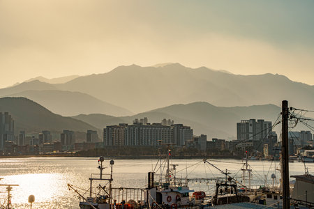 Beautiful sunset view of Sokcho harbor with fishing boats, expo tower, city skyline, and mountains in the background.の写真素材