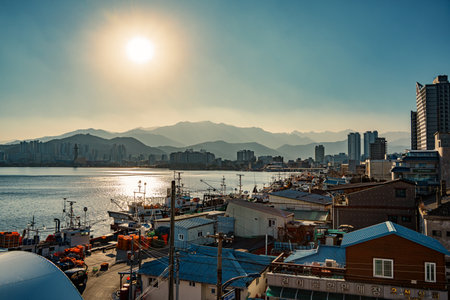 Beautiful sunset view of Sokcho harbor with fishing boats, expo tower, city skyline, and mountains in the background.の写真素材