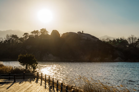 Beautiful sunset view over Yeongrang Lake with rocky island, trees, and mountain silhouette in background.の写真素材