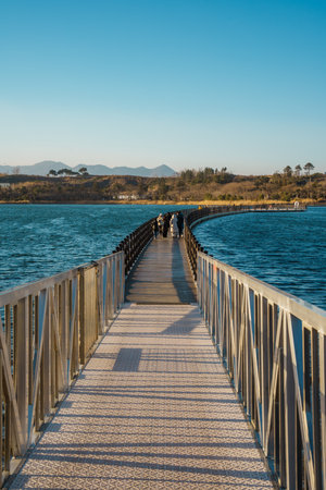 Long floating bridge stretching across Yeongrang Lake with mountain backdrop and clear blue sky.の写真素材