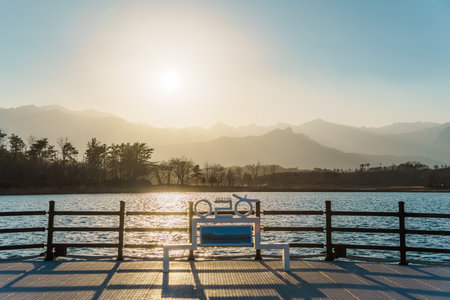 Warm sunset light over rippling water and layered mountain silhouettes from a lakeside viewing bench...