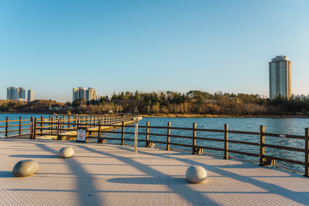 Wide lakeside boardwalk with wooden railing and city towers along Yeongrang Lake in Sokcho, South...