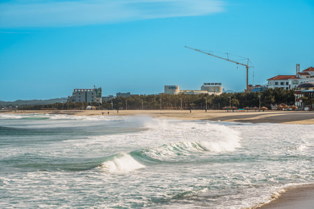 Curling swell lines approach the sandy shore at Naksan Beach, with a distant seaside building along...