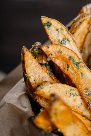 fried potatoes in an iron bucket with greens and sauce on a dark wooden backgroundの写真素材